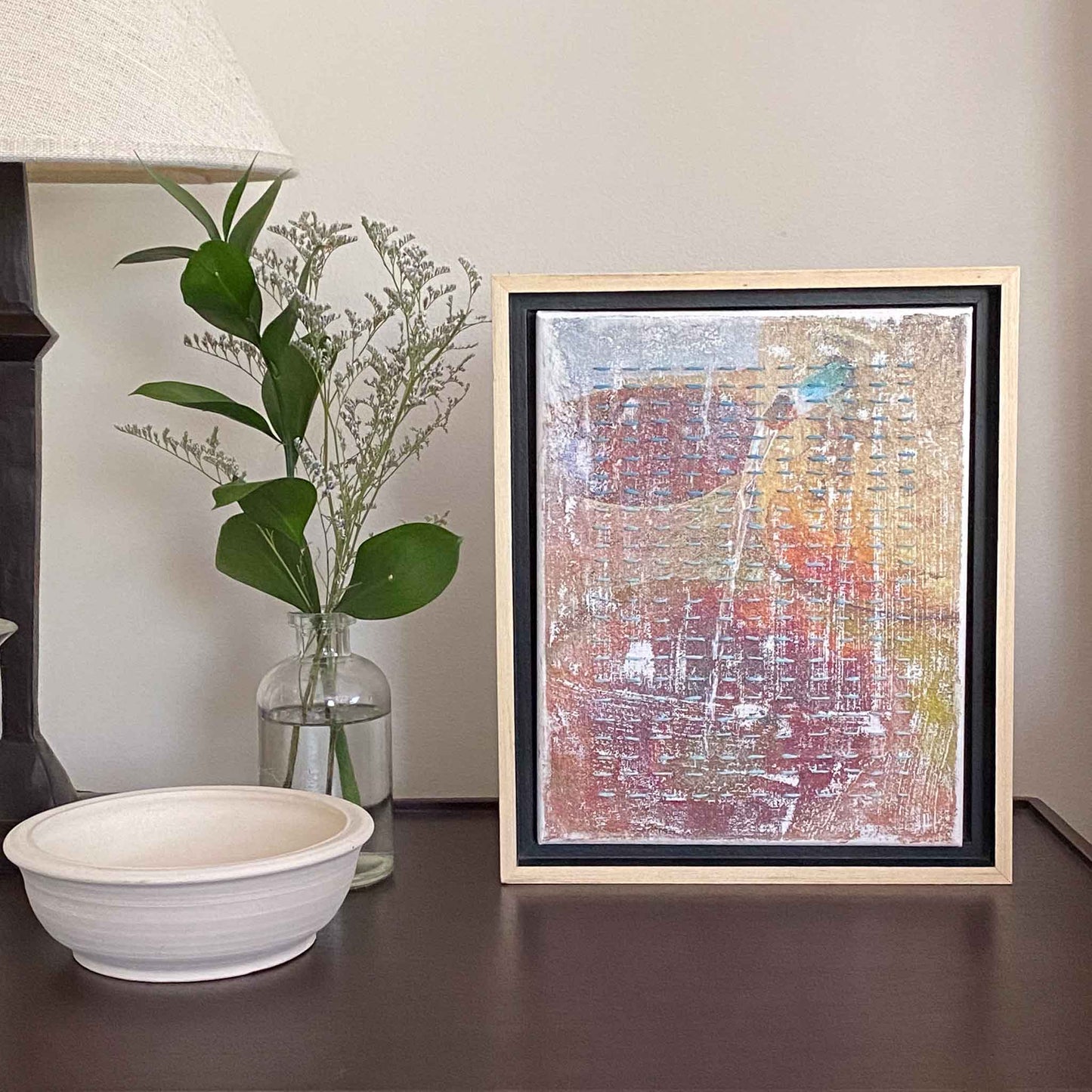 Framed artwork photo of Congress Spring with overlaid blue ombrage lines of embroidery on a shelf with a vase of foliage.