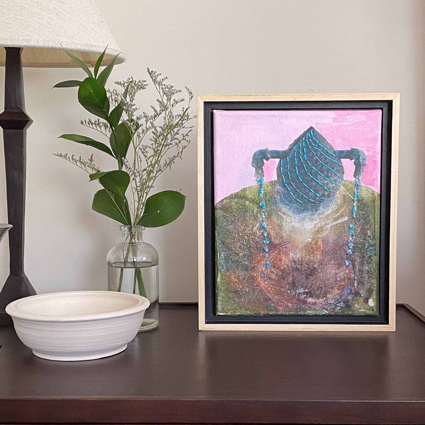Saratoga Springs Victorian Spring photo with a pink acrylic painted sky and embroidered blue spring water on a shelf beside a vase of flowers and foliage.